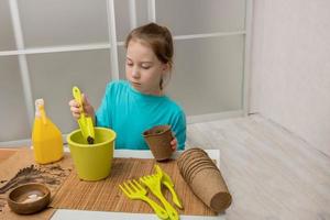 mignonne peu fille avec enthousiasme verse le Terre dans tourbe des pots pour semis photo