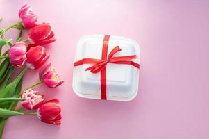 brillant coloré éponge rouge tulipes mensonge sur une rose Contexte sur le côté de une blanc gâteau boîte. photo