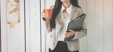affaires femme en portant café tasse et portefeuille dans bureau. photo
