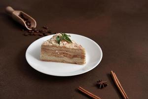 délicieux napoléon gâteau avec crème sur une blanc assiette décoré avec une brin de menthe sur une marron Contexte. une cannelle bâton, Badyan, café des haricots sur une marron Contexte. copie espace photo