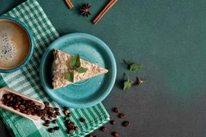 Haut vue de délicieux napoléon gâteau avec crème sur une turquoise assiette décoré avec une brin de menthe sur une vert Contexte. une tasse de chaud café, cannelle bâton, Badyan, café des haricots sur une vert motif photo