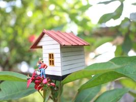 une proche en haut de une miniature figure de une mère arrosage le les plantes dans de face de le maison. photo