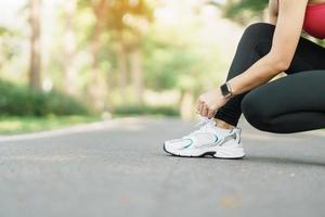 Jeune athlète femme attacher fonctionnement des chaussures dans le parc Extérieur, femelle coureur prêt pour le jogging sur le route dehors, asiatique aptitude en marchant et exercice sur sentier dans Matin. bien-être et sport concepts photo