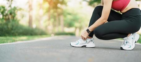 Jeune athlète femme attacher fonctionnement des chaussures dans le parc Extérieur, femelle coureur prêt pour le jogging sur le route dehors, asiatique aptitude en marchant et exercice sur sentier dans Matin. bien-être et sport concepts photo