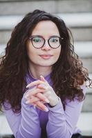 magnifique Jeune femme avec brunette frisé cheveux, portrait dans œil des lunettes profiter le Soleil dans le ville. photo