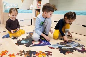 enfants connectant des pièces de puzzle dans une chambre d'enfants au sol à la maison. loisirs amusants en famille. photo