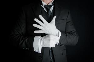 portrait de majordome en costume sombre sur fond noir tirant sur des gants blancs propres. concept d'industrie de services et d'hospitalité professionnelle. photo