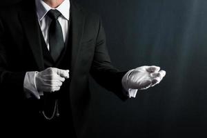 portrait de majordome dans foncé costume et blanc gants offre portion main. concept de un service industrie et professionnel courtoisie. photo