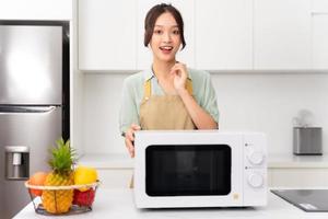 asiatique fille permanent suivant à le four micro onde dans sa cuisine photo