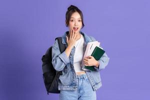 portrait de une magnifique asiatique écolière portant une sac à dos sur une violet Contexte photo