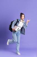 portrait de une magnifique asiatique écolière portant une sac à dos sur une violet Contexte photo