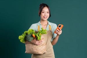 asiatique fille portrait en portant une sac de des légumes sur une vert Contexte photo