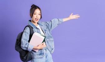 portrait de une magnifique asiatique écolière portant une sac à dos sur une violet Contexte photo