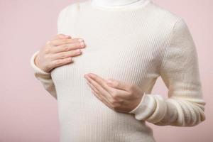 femme mains vérification grumeaux sur sa Sein pour panneaux de Sein cancer sur rose Contexte. soins de santé monde santé journée concept. photo