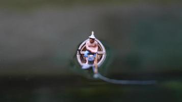 miniature figure de une pêcheur pêche sur une Lac dans une petit bateau. photo