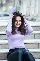 magnifique Jeune femme avec brunette frisé cheveux, portrait dans œil des lunettes profiter le Soleil dans le ville. photo