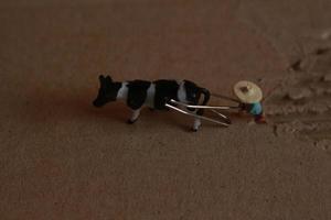 miniature figure de une agriculteur labour une champ avec le sien vache sur une papier carton. photo