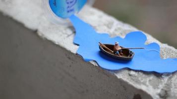 une miniature figure de une pêcheur pêche dans une rivière visualisé sur bleu papier découpes. photo