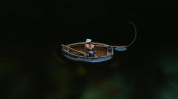 miniature figure de une pêcheur pêche sur une Lac dans une petit bateau. photo