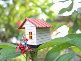 une proche en haut de une miniature figure de une mère arrosage le les plantes dans de face de le maison. photo