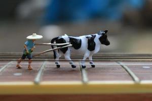 miniature figure de une agriculteur labour une champ avec le sien vache sur une guitare. photo