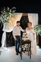 les jeunes mariés coupent et goûtent joyeusement le gâteau de mariage photo