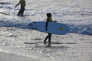 surfeurs avoir prêt à entrer le l'eau et en marchant avec le planche le long de le rive. photo