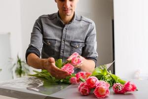 homme fleuriste fait du rouge tulipe bouquet et emballage dans pack sur en bois tableau. fleurs photo
