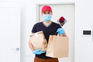 livreur tenant un sac en papier avec de la nourriture sur fond blanc, livreur de nourriture dans un masque de protection et des gants de protection photo