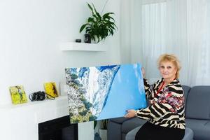 une content personnes âgées blond femme est en portant une grand mur photo Toile à Accueil