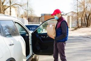 livraison par auto. homme dans protecteur masque et médical gants en portant une papier boîte. livraison un service en dessous de quarantaine, maladie épidémie, coronavirus covid-19 pandémie conditions. photo