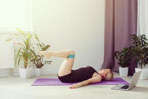 seul fille Faire yoga des exercices en ligne sur portable sur le sol dans le lumière chambre, rester Accueil sûr monde. photo