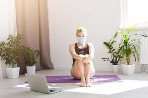 seul fille dans médical masque Faire yoga des exercices sur le sol dans le lumière pièce pendant quarantaine de convoitise 19 cotonavirus rester Accueil sûr monde. photo