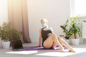 seul fille dans médical masque Faire yoga des exercices sur le sol dans le lumière pièce pendant quarantaine de convoitise 19 cotonavirus rester Accueil sûr monde. photo