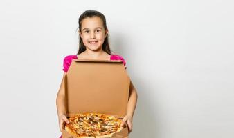 mignonne peu Indien asiatique fille enfant en mangeant savoureux Pizza dans boîte. permanent isolé plus de blanc Contexte. photo