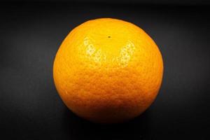 des oranges sur une noir Contexte. un Orange est Couper dans moitié, le autre est ensemble. photo