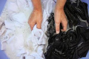 femelle main laver noir et blanc vêtements dans même bassin. photo