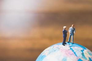 Hommes d'affaires miniatures debout sur une carte du monde globe avec un fond brun photo