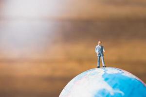 homme d'affaires miniature debout sur une carte du monde globe avec un fond marron photo