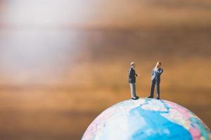 Hommes d'affaires miniatures debout sur une carte du monde globe avec un fond brun