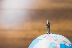 homme d'affaires miniature debout sur une carte du monde globe avec un fond marron photo