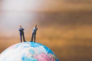 Hommes d'affaires miniatures debout sur une carte du monde globe avec un fond brun photo