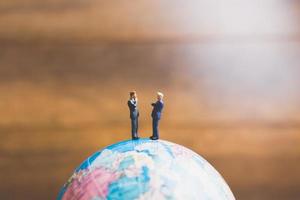 Hommes d'affaires miniatures debout sur une carte du monde globe avec un fond brun photo