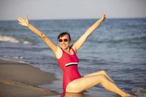 content femme à le mer dans le Soleil. femme dans une maillot de bain éclaboussures l'eau sur une Contexte de vagues. été vacances sur le plage. photo