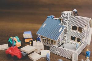 Travailleurs miniatures réparant une maison sur un fond de bois photo