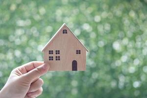 Main de femme tenant une maison modèle sur fond vert naturel, investissement commercial et concept immobilier