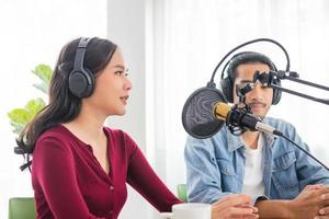 sourire deux jeunes femmes asiatiques, hommes animateurs de radio dans les écouteurs, microphone tout en parlant, conversation, enregistrement de podcast en diffusion au studio ensemble. technologie de création de concept audio d'enregistrement. photo