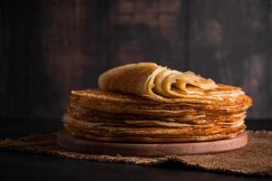 une pile de crêpes minces sur un fond en bois foncé. un plat traditionnel de crêpes pour la maslenitsa de vacances. photo