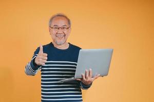 asiatique Sénior homme en utilisant portable ordinateur pour travail après retraite sur le Jaune Contexte. photo