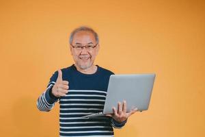 asiatique Sénior homme en utilisant portable ordinateur pour travail après retraite sur le Jaune Contexte. photo